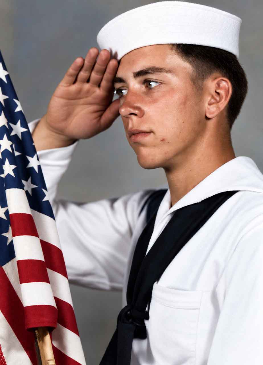 A colourised and restored image of Gunner's Mate ,2nd Class, Felton Thomas Fitts, in uniform, saluting beside the American national flag.