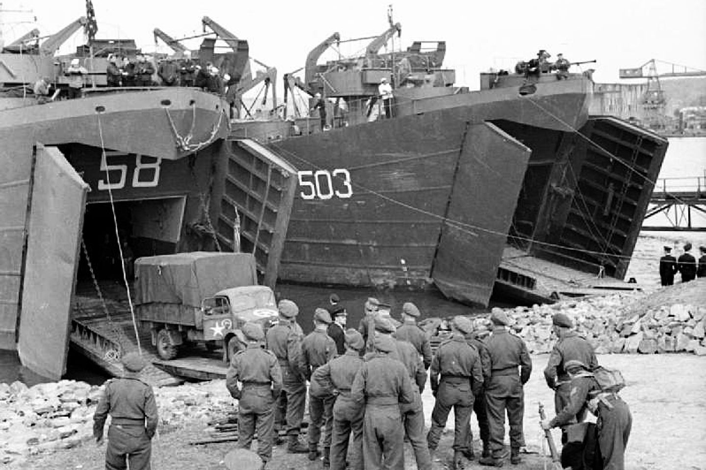 British troops watching lorries being loaded aboard USS LST-58 with USS LST-503 alongside.